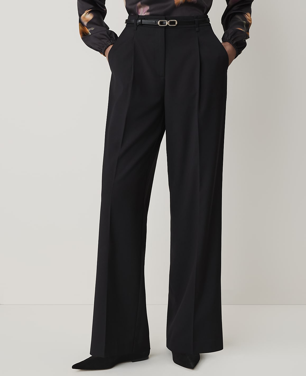 A person stands in black wide-leg pants and a patterned blouse against a plain white background.