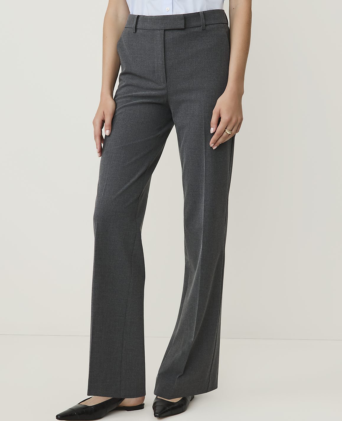 A person in grey dress pants and black slingback shoes stands against a plain white background.