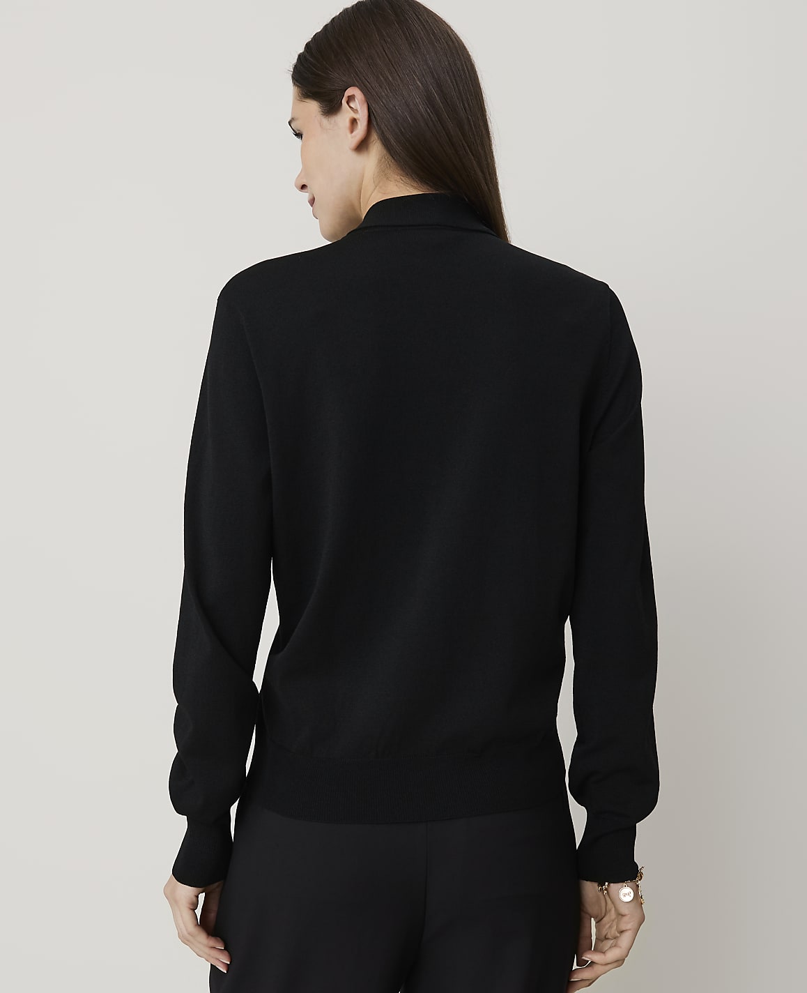 A woman in a black turtleneck sweater and pants stands against a plain white background.