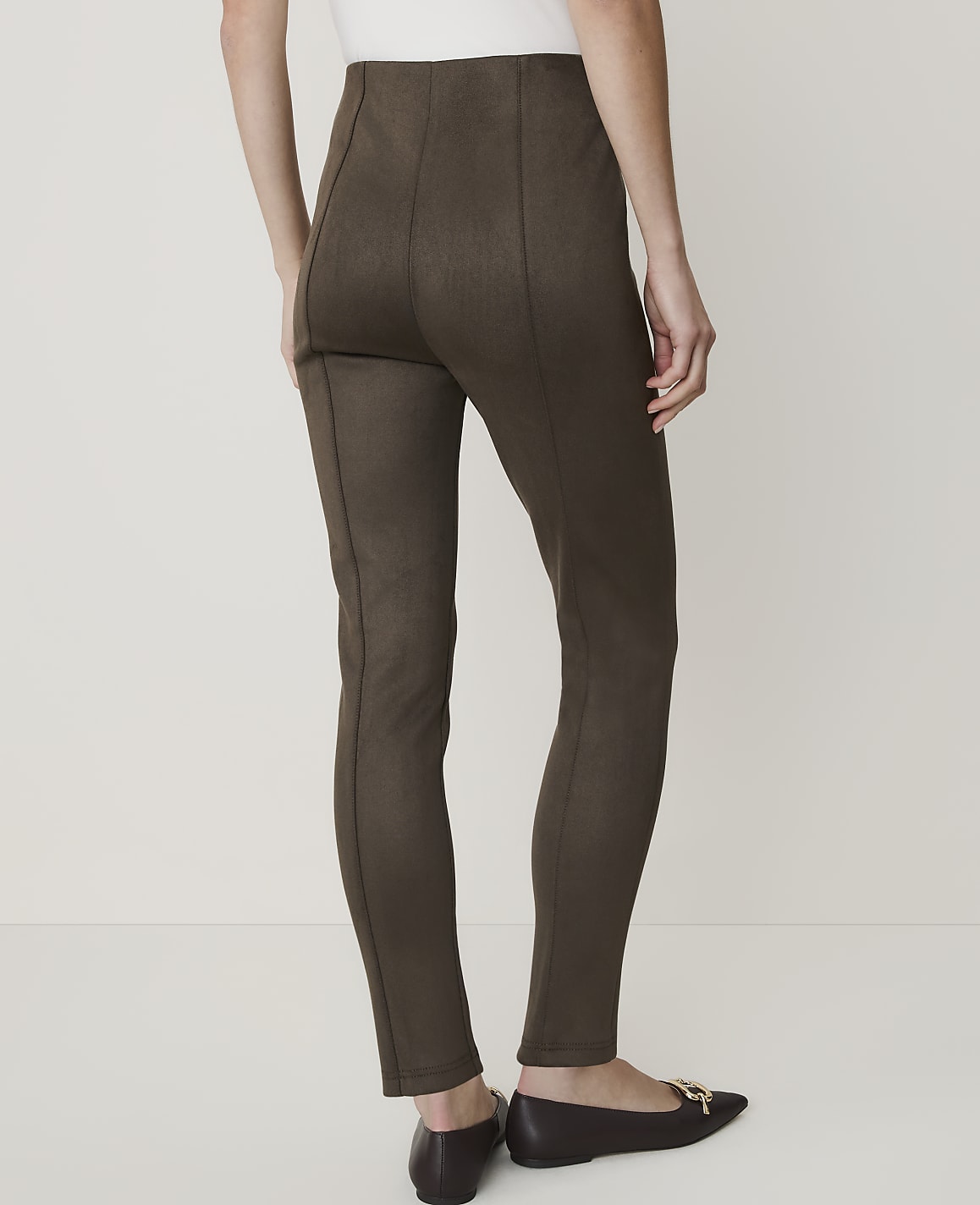 A person wearing brown leggings and brown flats stands against a plain white background.