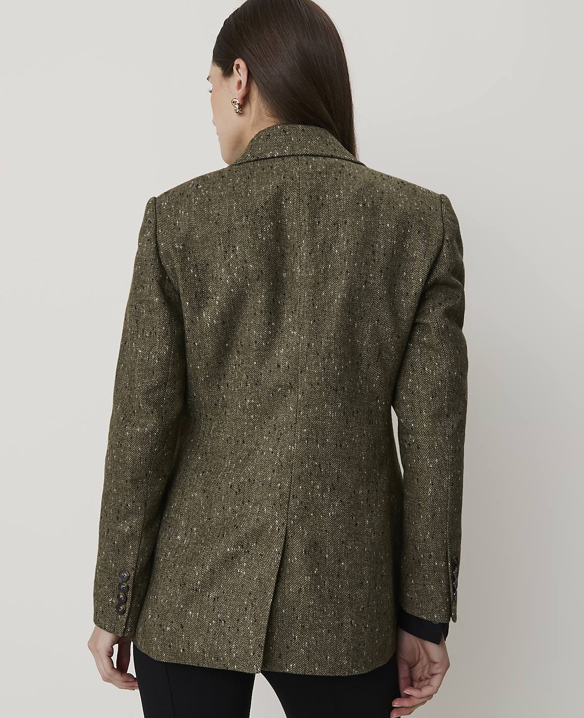A woman in a textured green blazer stands against a plain, light-colored background.