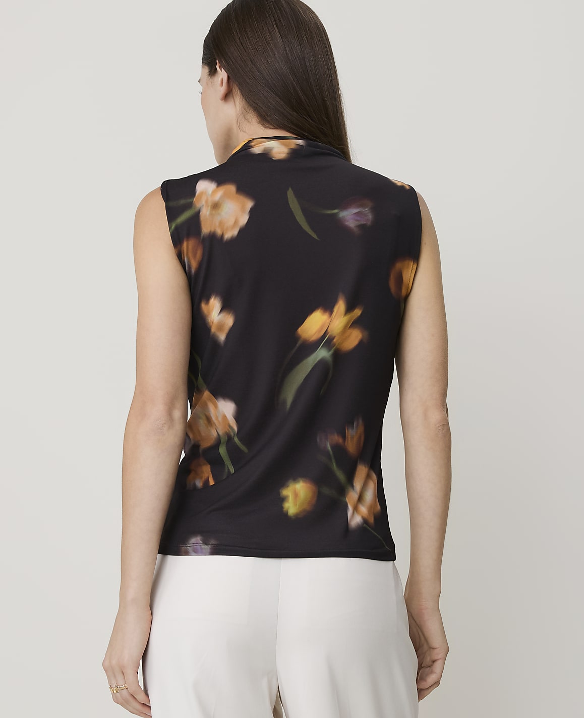 A woman in a black floral-print sleeveless top stands against a blurred background.