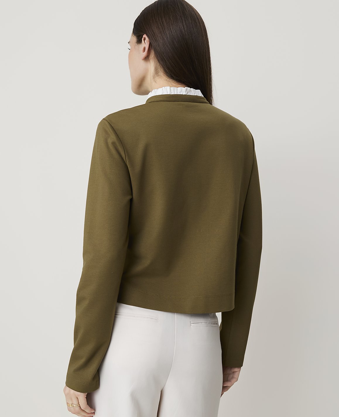 A woman in a green jacket and white pants stands against a plain white background.