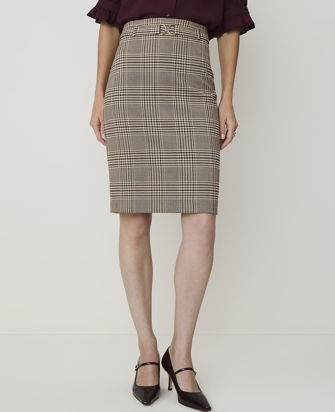 A woman models a brown plaid pencil skirt and dark heels against a plain white background.