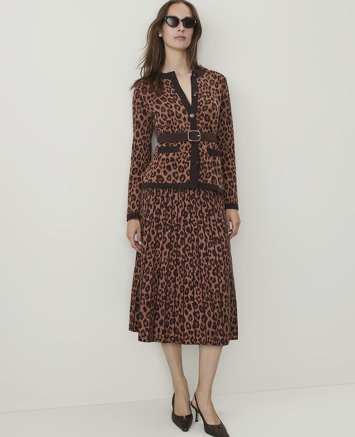 A woman in a leopard-print cardigan and skirt stands against a plain, light-colored background.