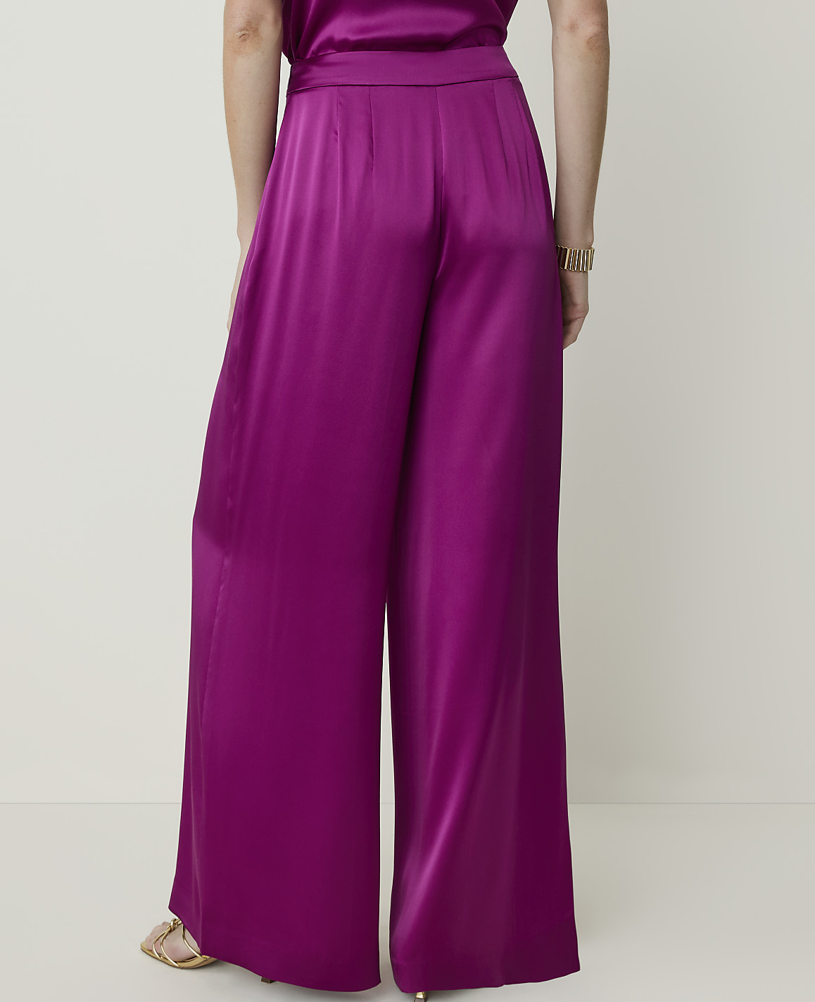 A person wearing wide-leg magenta satin pants stands against a plain, light-colored background.