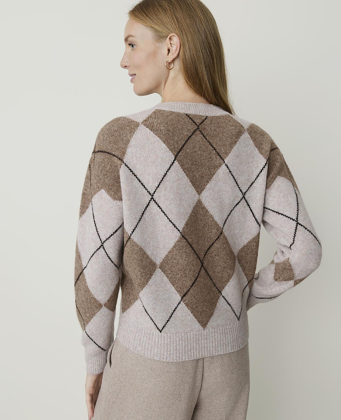 A woman in a tan argyle sweater stands against a plain, light-colored background.