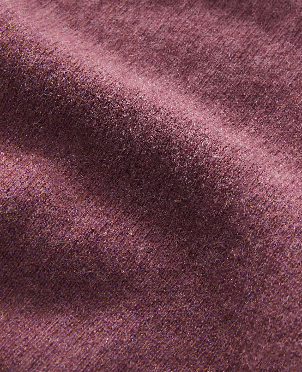 A close-up of a textured, rose-colored fabric with soft folds fills the frame, with no discernible background.