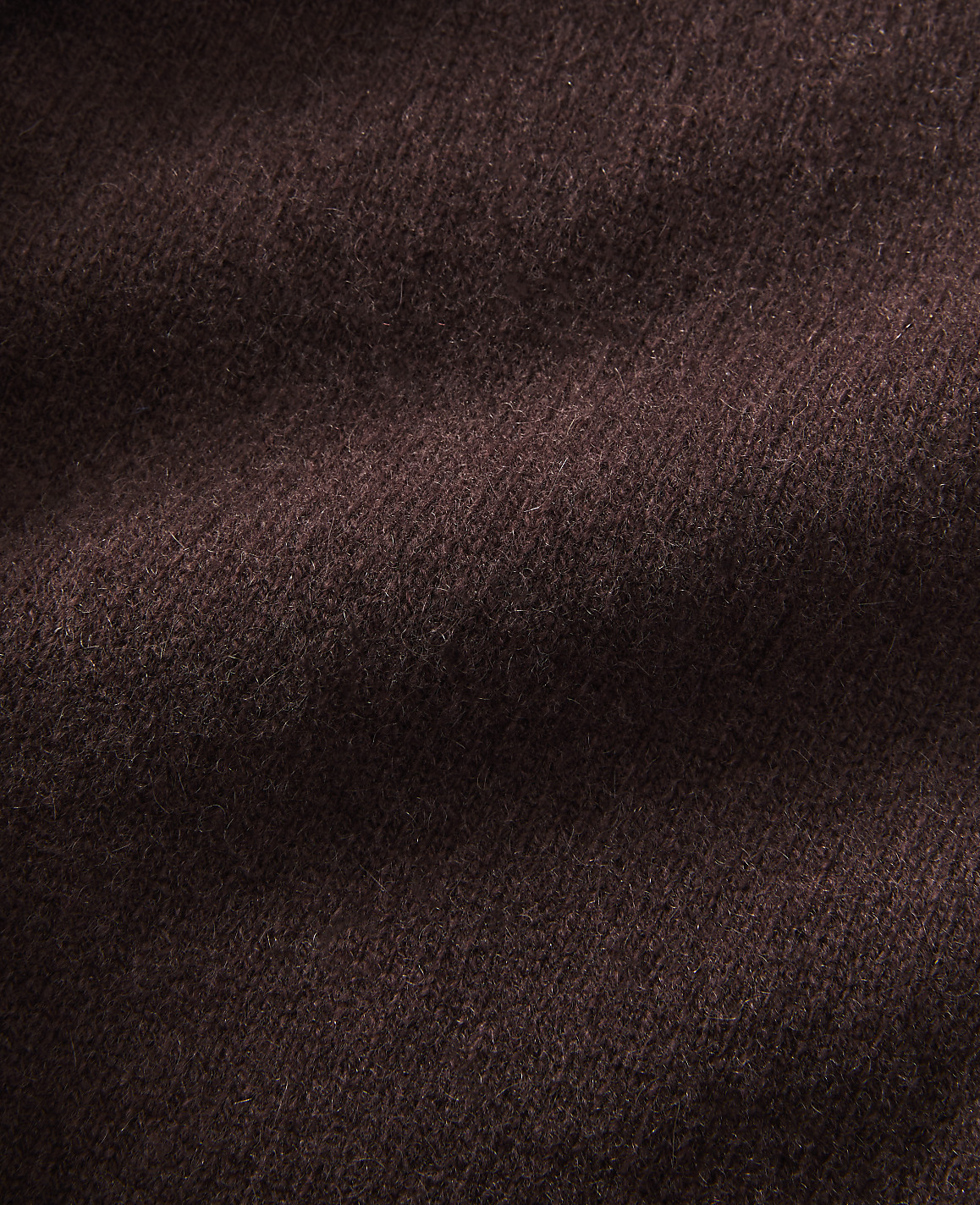 A close-up view of dark brown, textured fabric fills the frame, with soft folds and shadows creating depth.