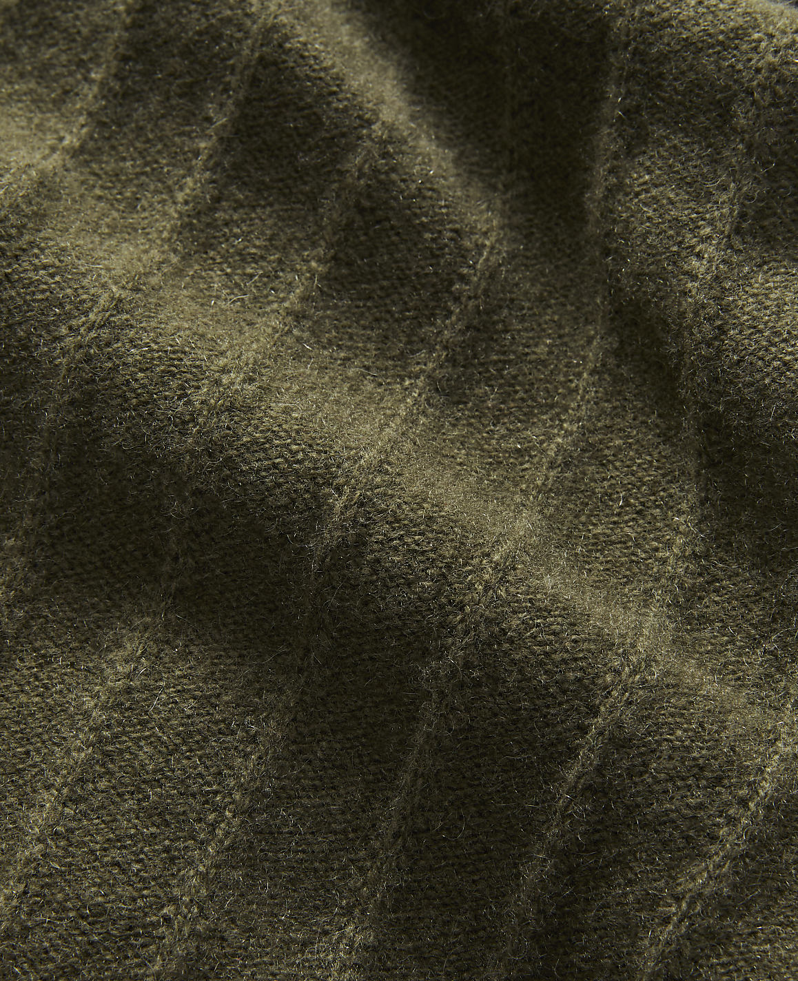 A close-up of textured olive-green fabric with diagonal ribbing fills the frame, with subtle shadows and highlights creating depth.