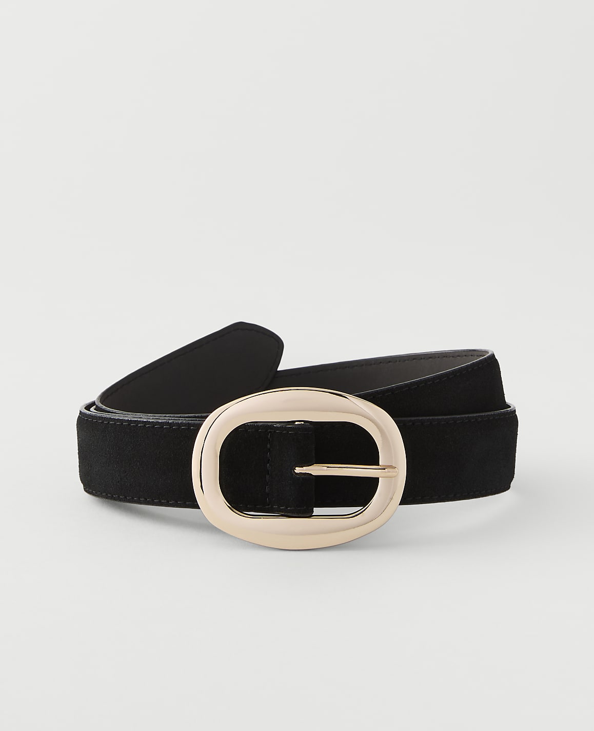 A black suede belt with a large, oval, rose gold buckle rests on a plain white background.