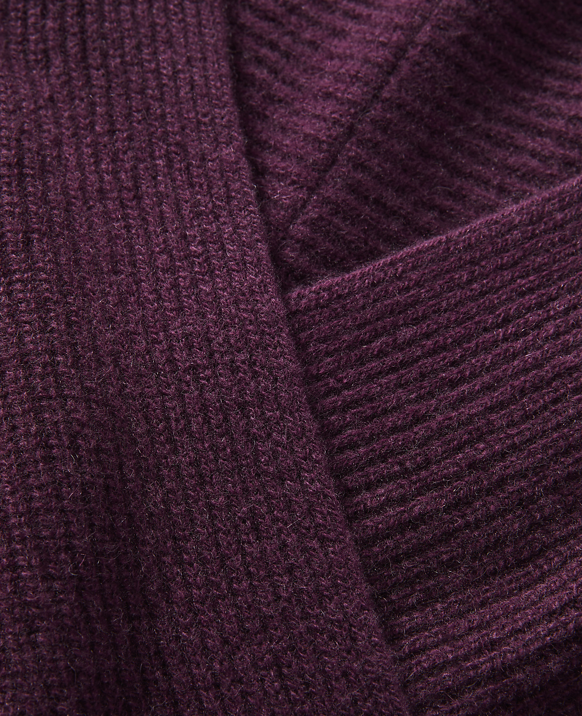 A close-up view of a ribbed, plum-colored knit fabric folds over itself, creating a textured background.