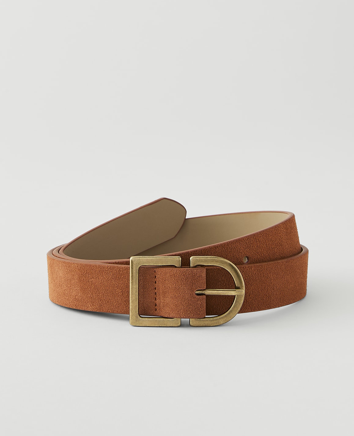 A rust-colored suede belt with a brass buckle lies on a plain, light gray background.