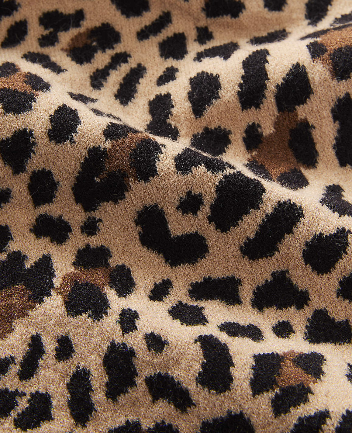 A close-up view of a tan fabric with a black and brown leopard print pattern fills the frame, with soft folds and textures visible throughout.