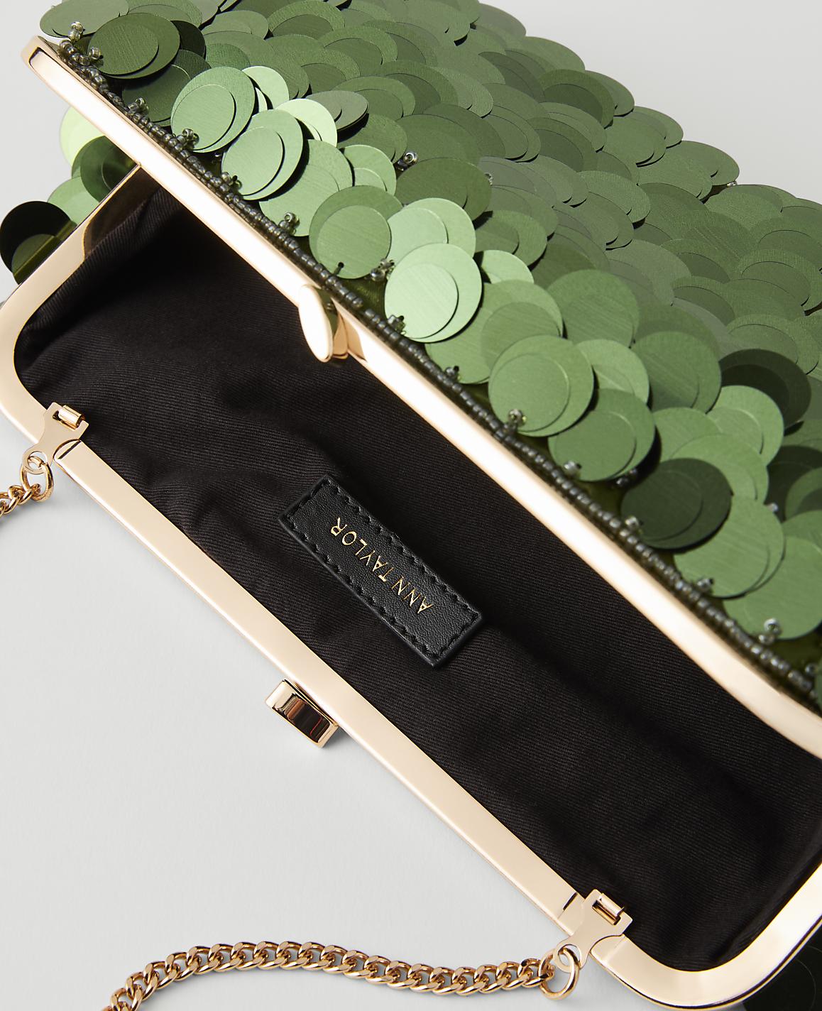 A green sequined clutch with a gold chain strap is open to reveal a black interior with a brand tag, set against a plain background.