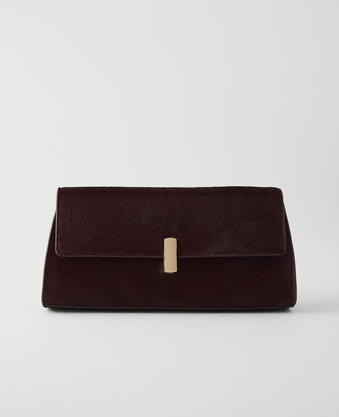 A dark red clutch with a gold clasp rests on a white surface against a plain white background.