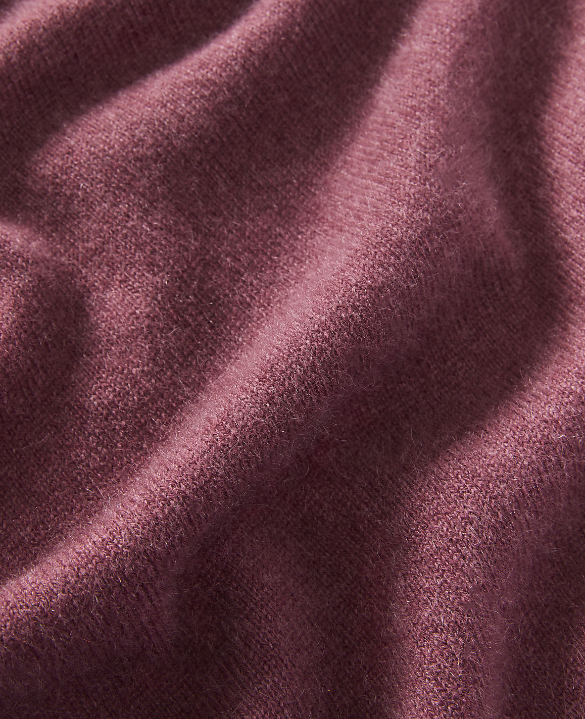 A close-up of a textured, rose-colored fabric with soft folds fills the frame, with no discernible background.