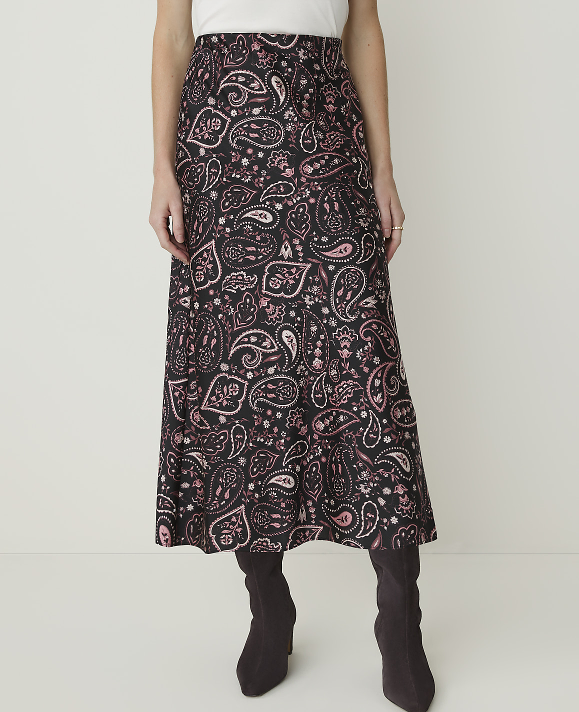 A woman in a black and pink paisley skirt and dark boots stands against a plain white background.