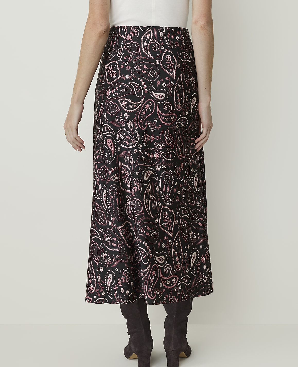 A woman in a black and pink paisley skirt and dark boots stands against a plain white background.