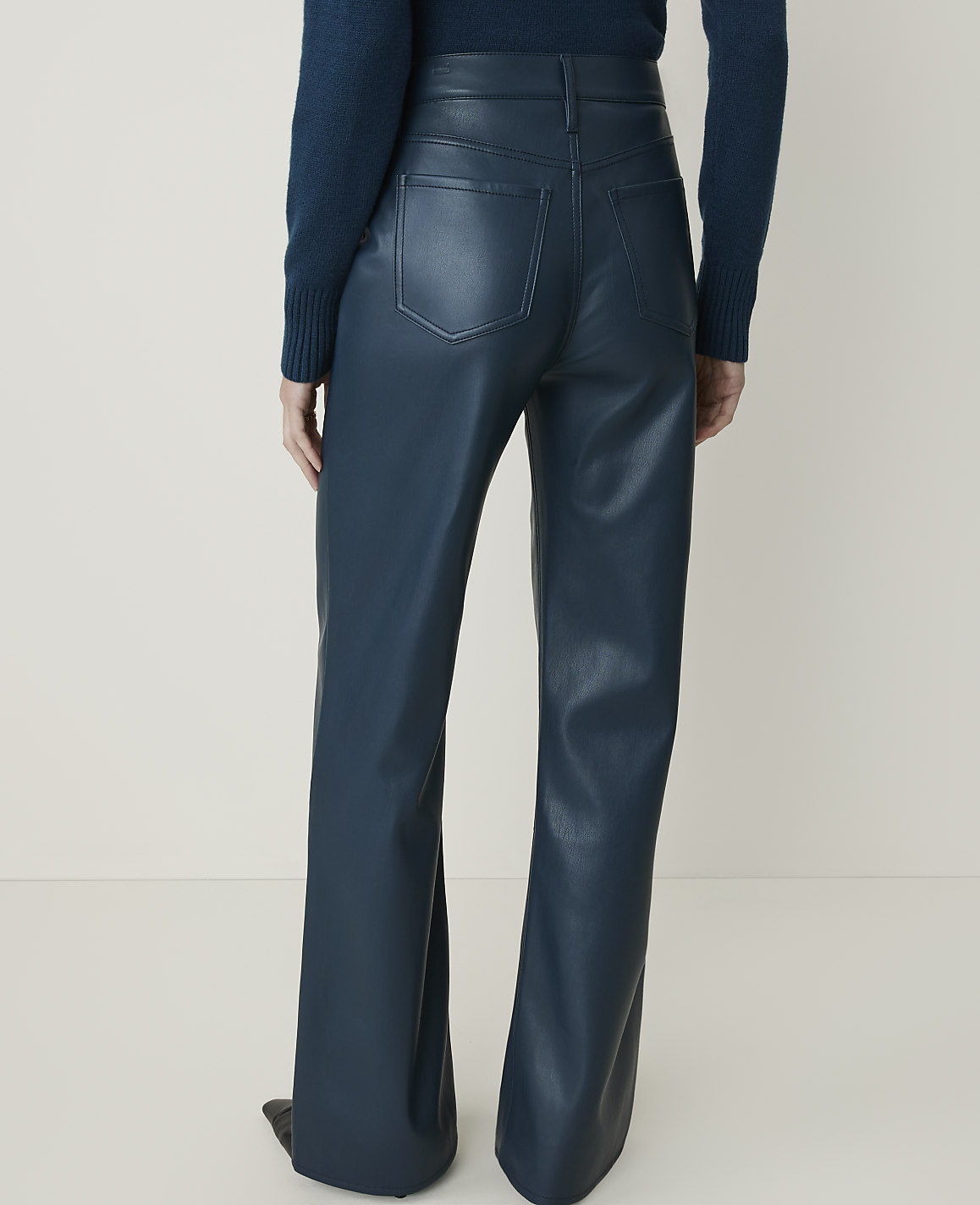 A person wearing teal faux leather flared pants stands against a plain, light-colored background.
