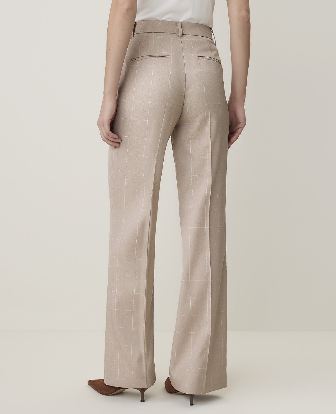 A person wearing beige wide-leg trousers stands against a plain, light-colored background.