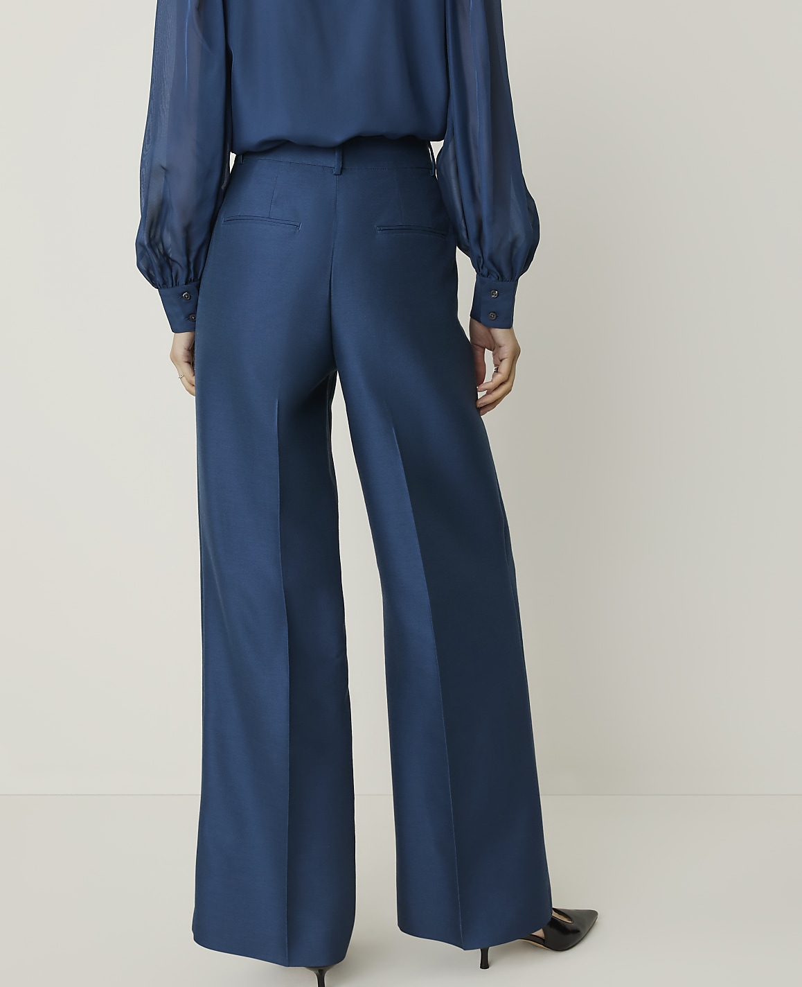 A person wearing a blue blouse and wide-leg blue pants stands against a plain white background.