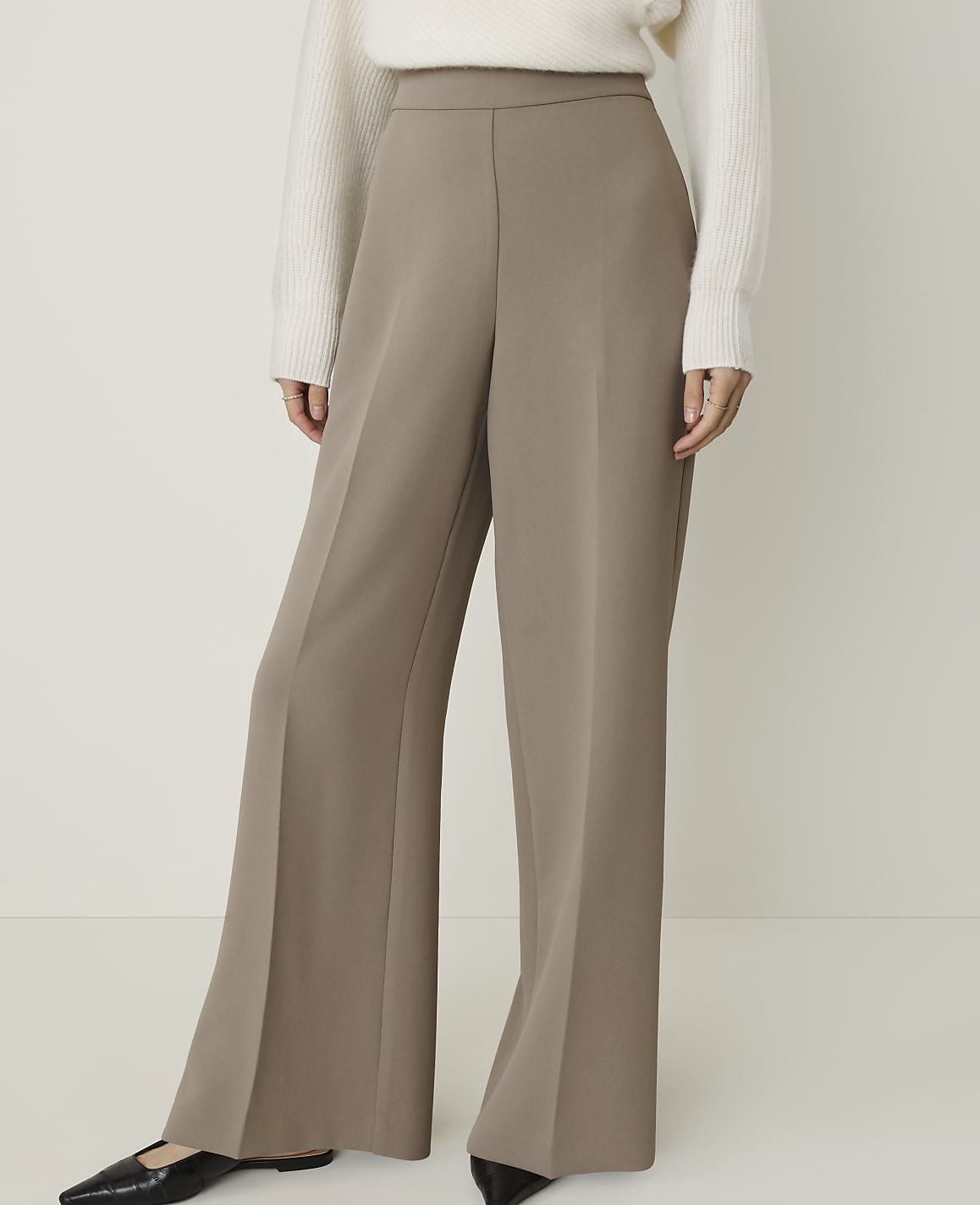 A person in a cream sweater and taupe wide-leg pants stands against a plain white background.