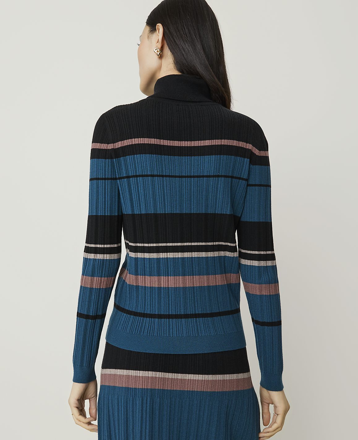 A woman in a striped turtleneck sweater stands against a plain, light gray background.
