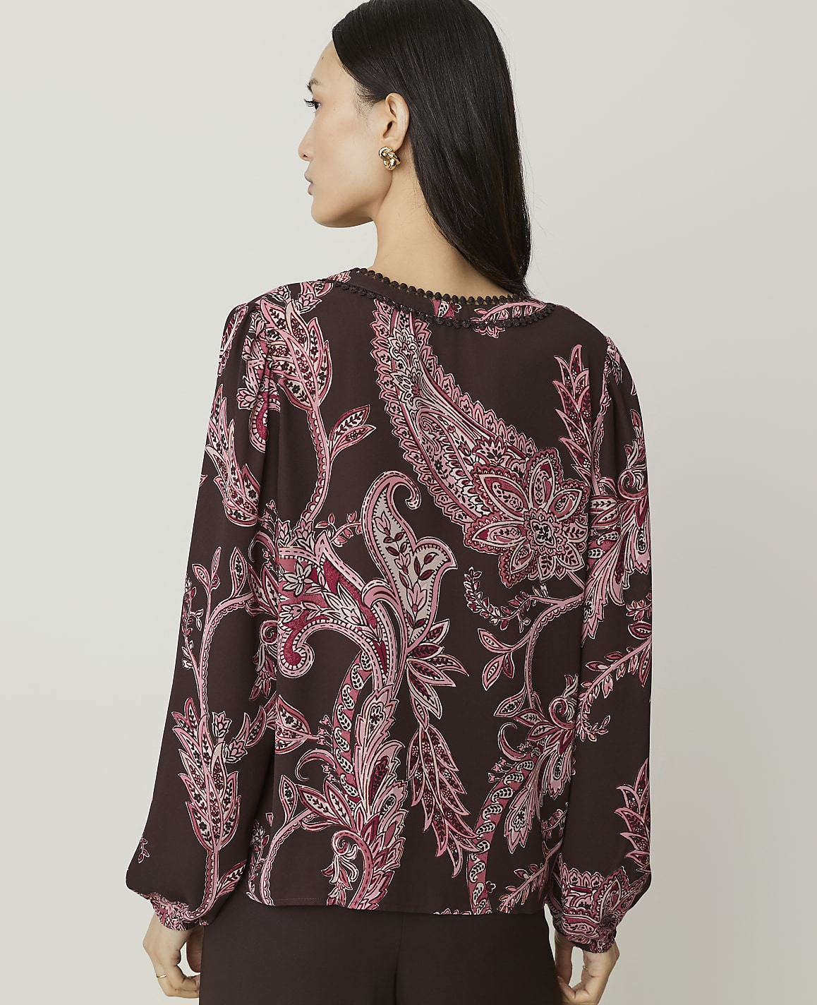 A woman in a brown paisley blouse stands against a plain background.