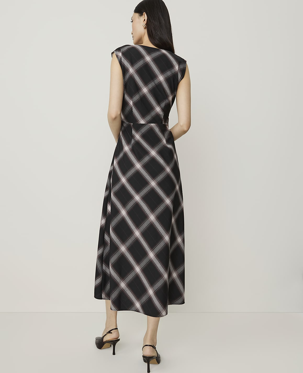 A woman in a plaid dress stands against a plain, light-colored background.