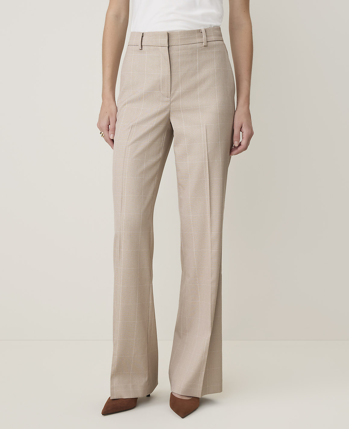 A person in beige pinstripe flared trousers and brown pointed-toe heels stands against a plain, light-colored background.