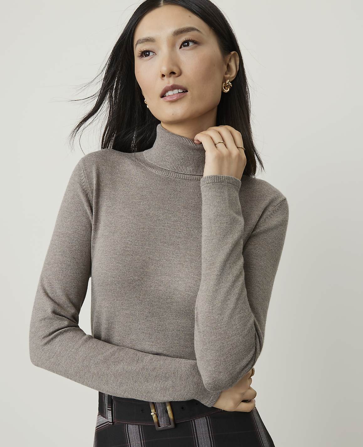A woman in a taupe turtleneck sweater poses against a plain white background.
