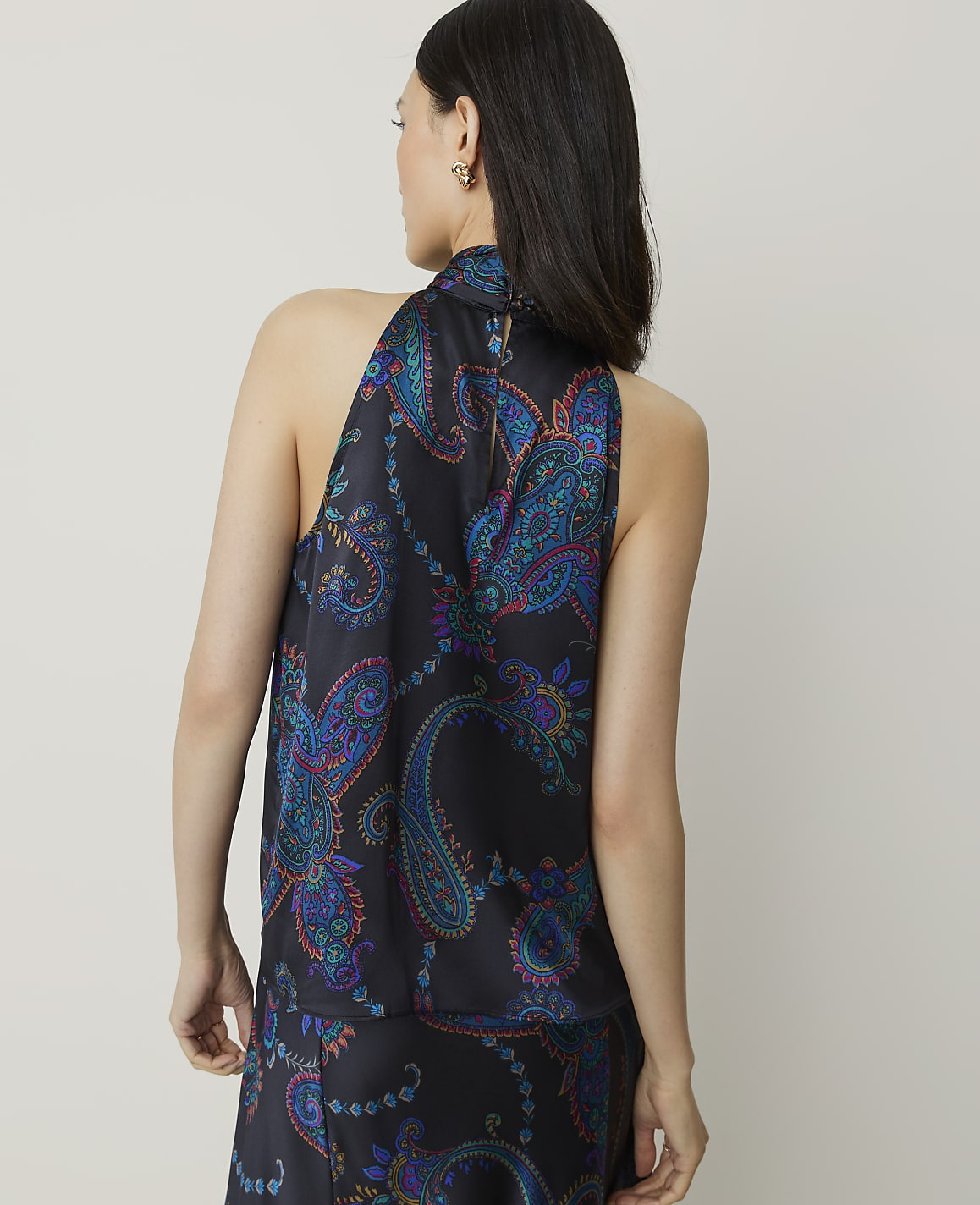 A woman in a dark, paisley-patterned halter top stands against a plain, light background.