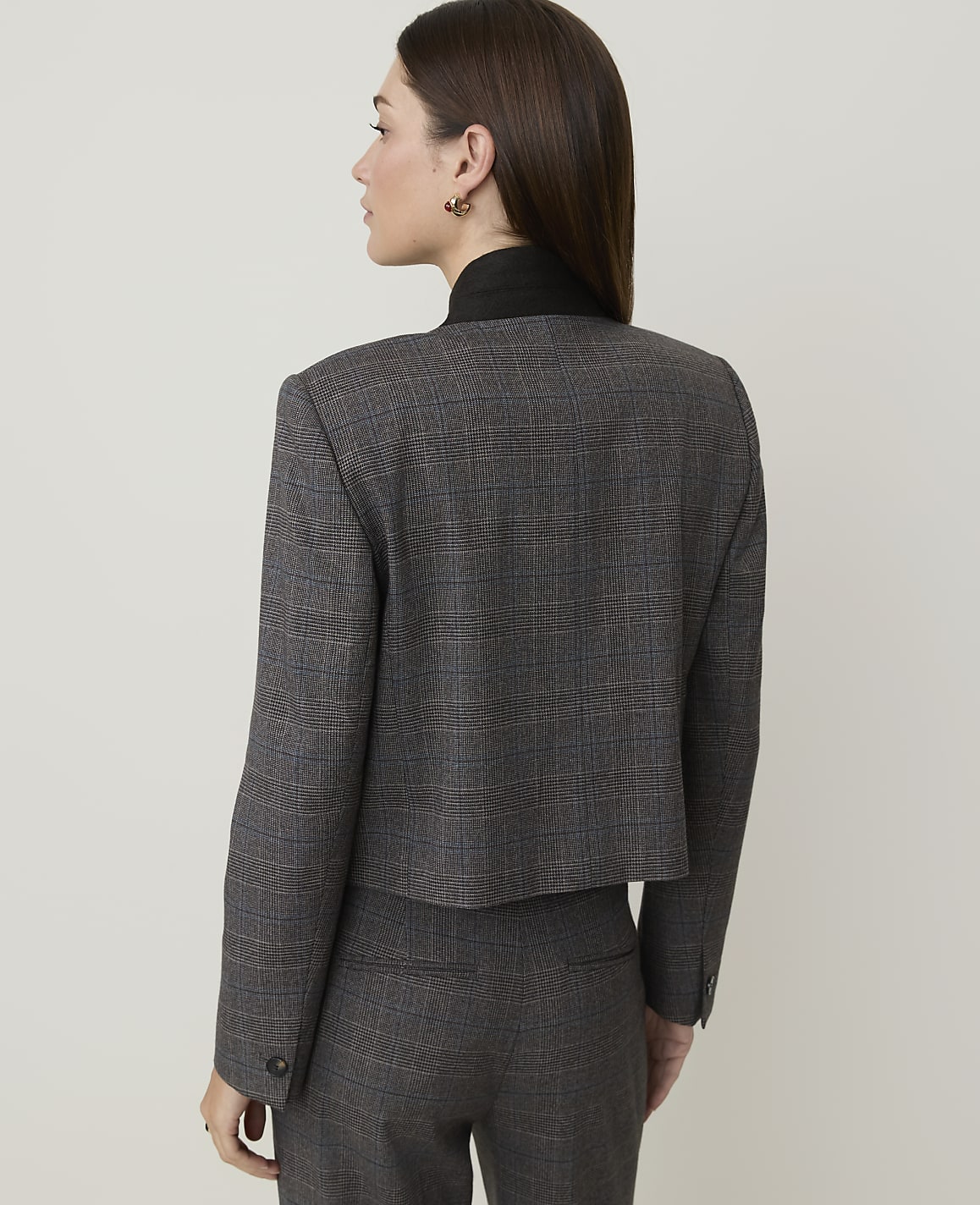 A woman in a plaid suit stands against a plain, light-colored background.