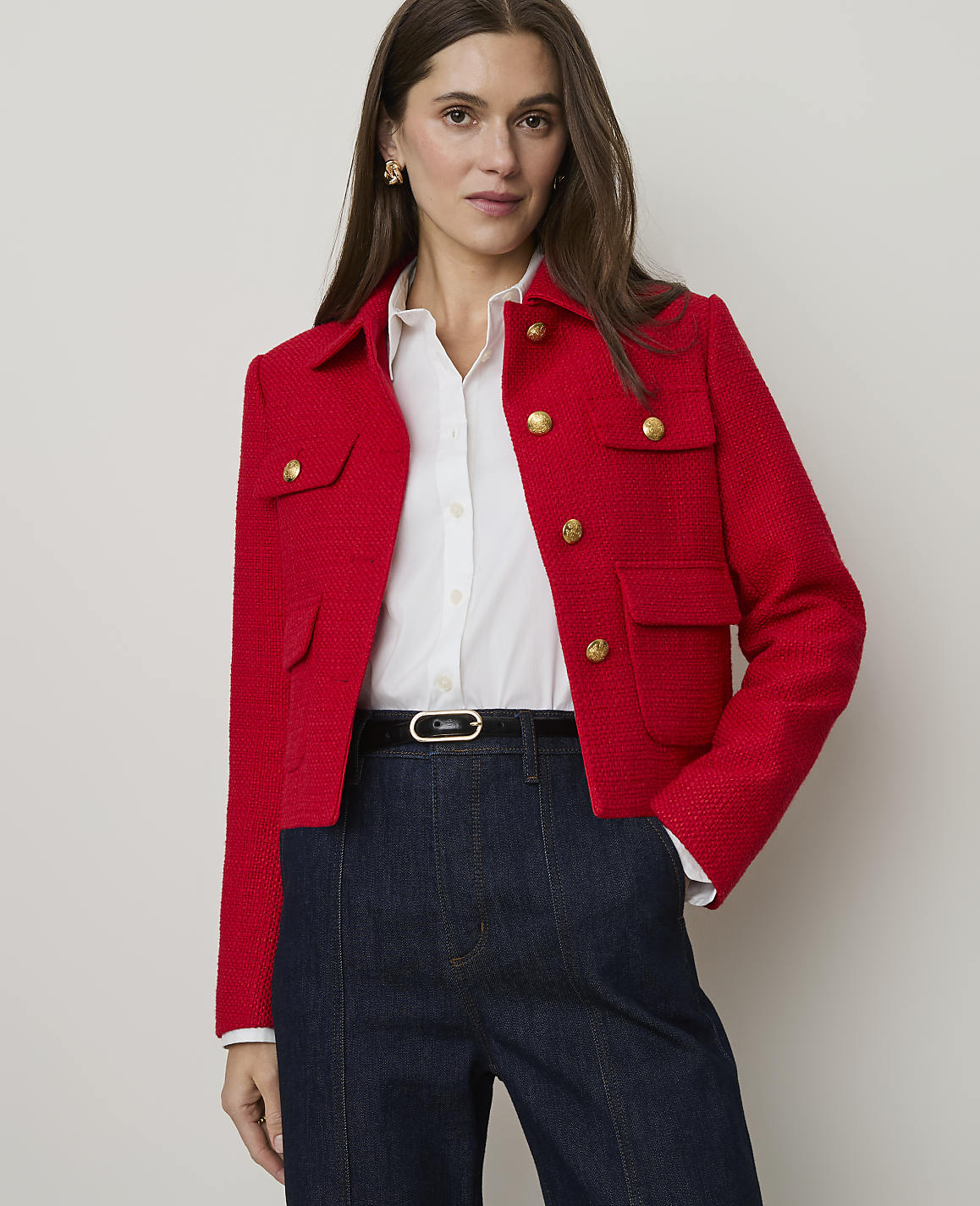 A woman in a red tweed jacket and skirt stands against a plain white background.