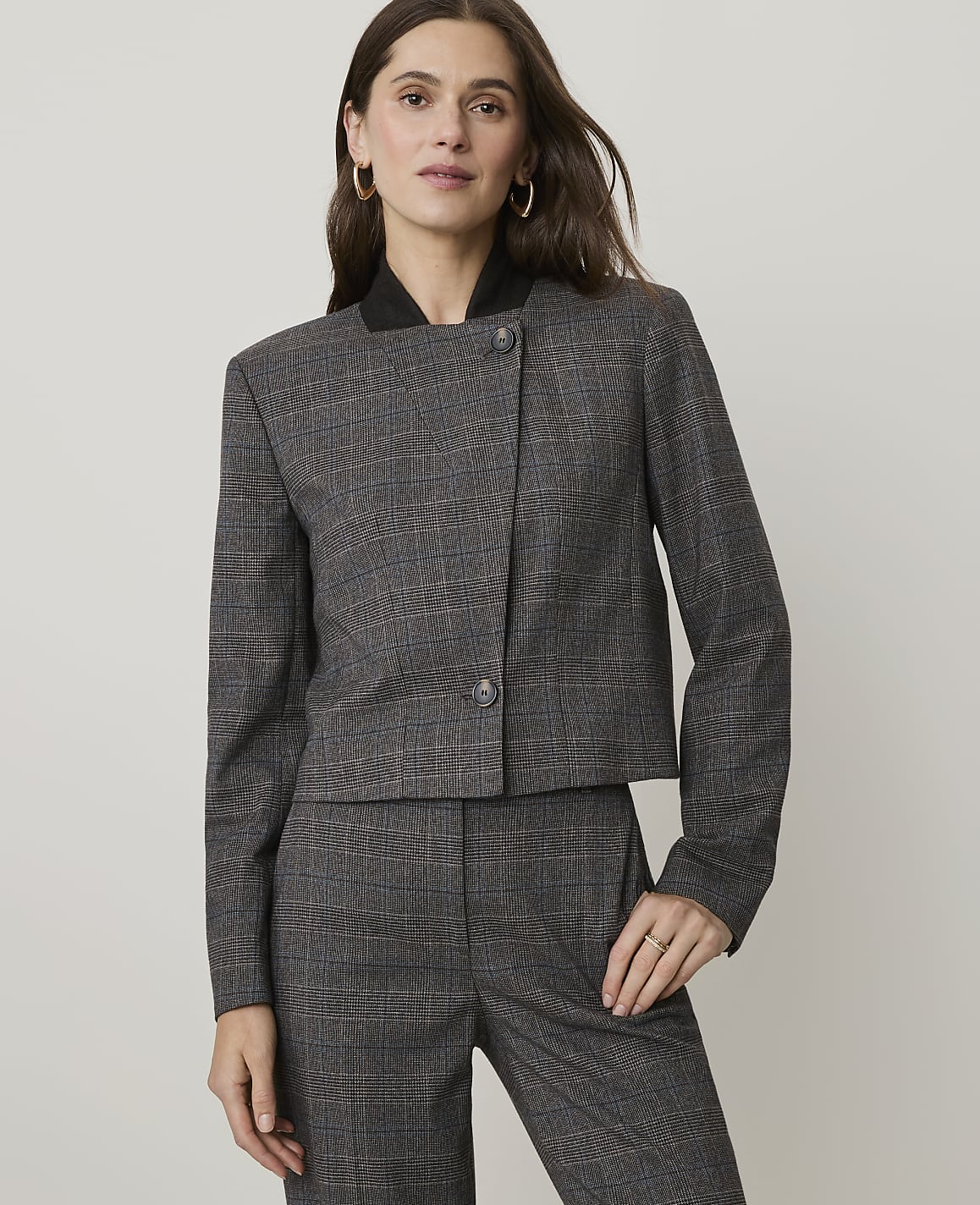 A woman in a plaid suit stands against a plain, light gray background.