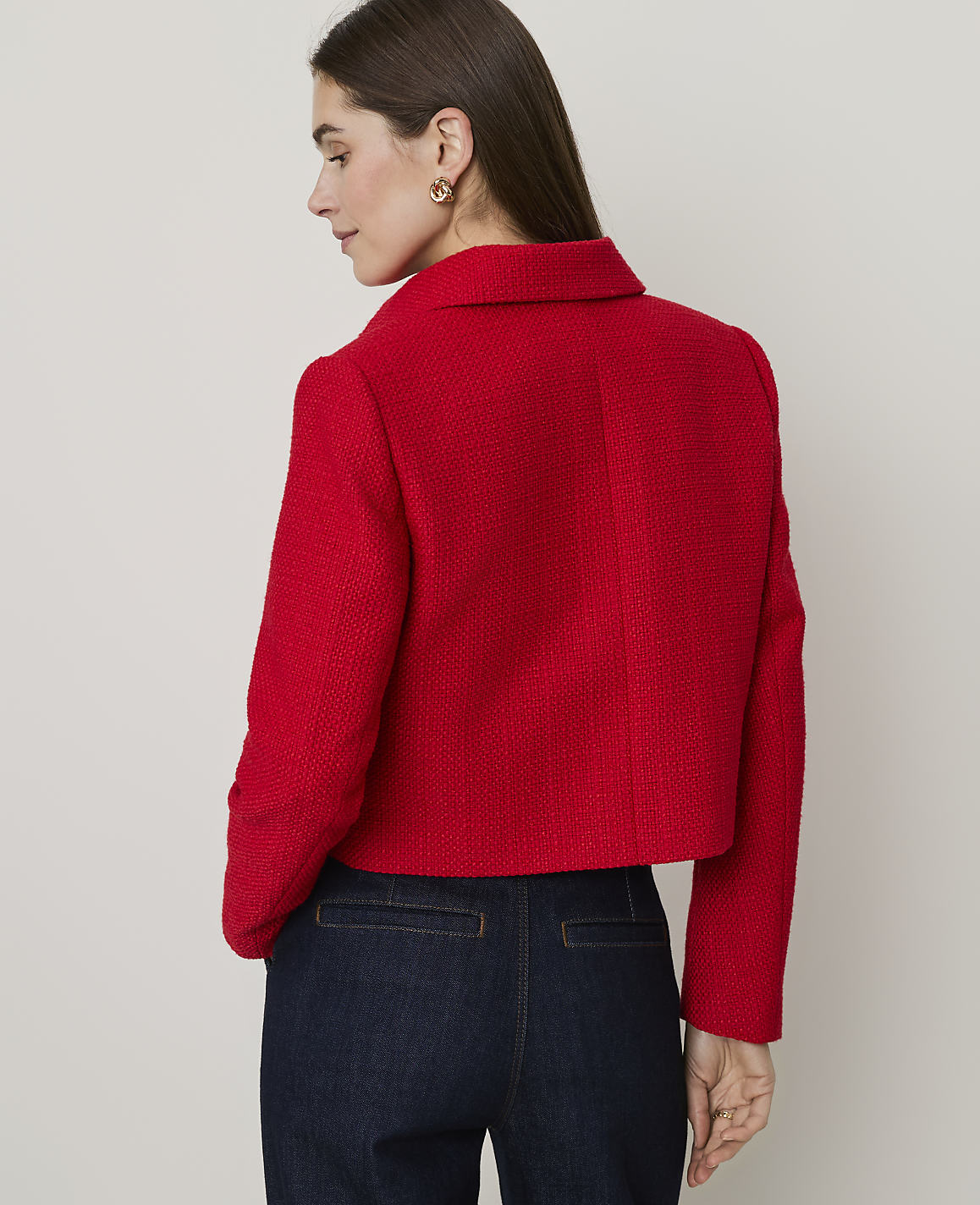 A woman in a red tweed jacket and skirt stands against a plain, light-colored background.