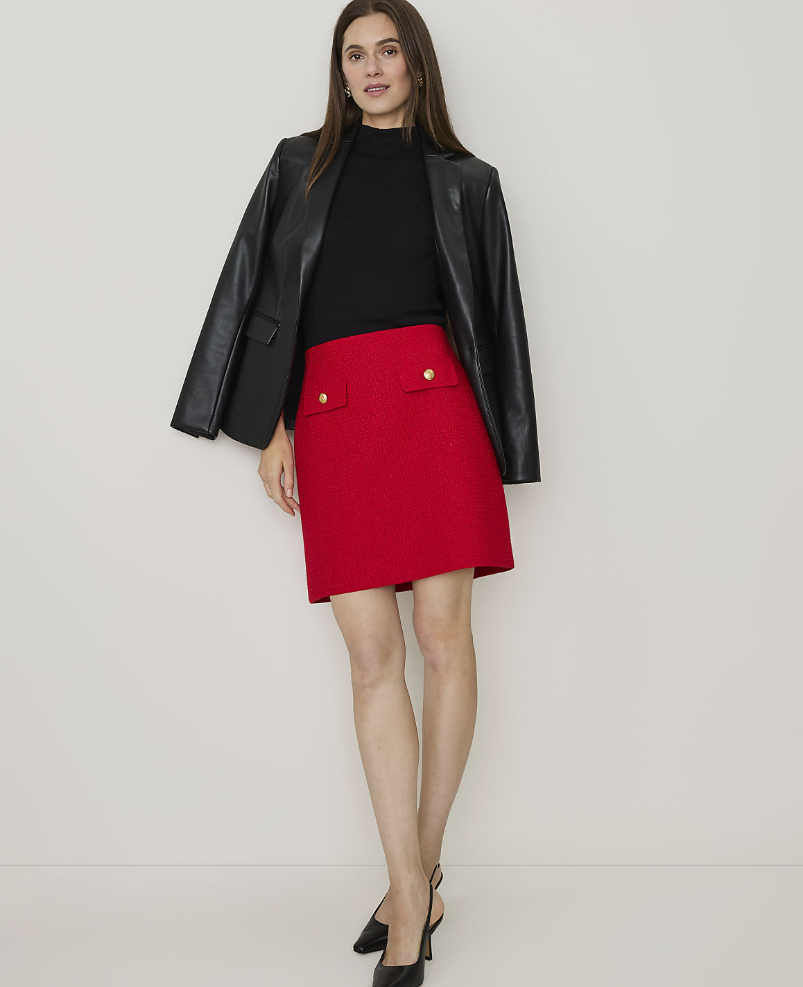 A woman in a red tweed skirt and black heels walks away from the camera against a plain white background.