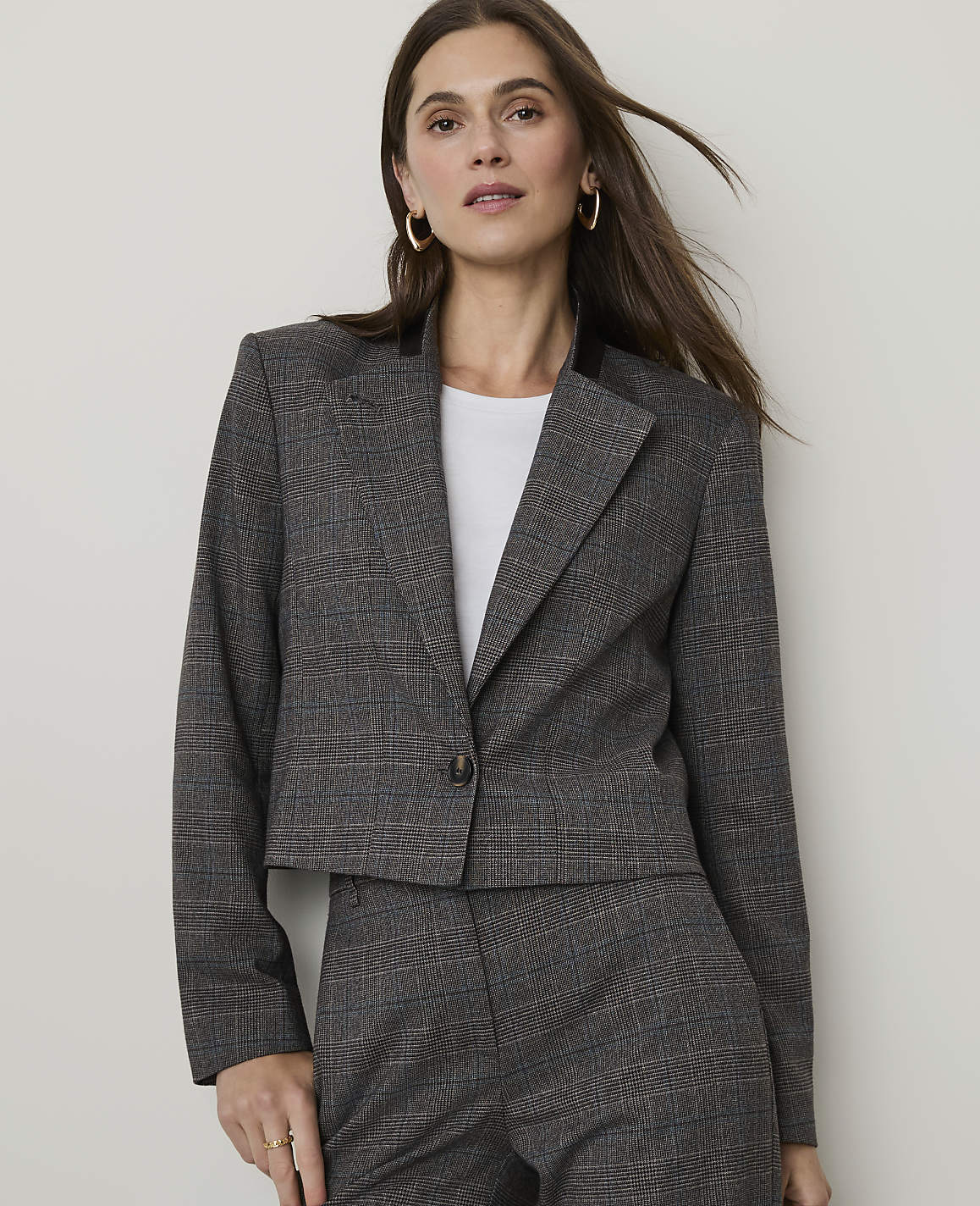 A woman in a plaid suit stands against a plain, light-colored background.