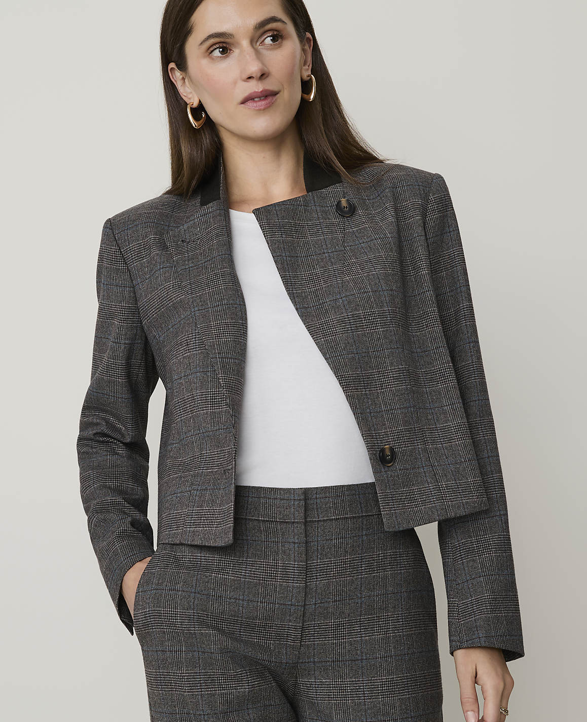 A woman in a plaid blazer and pants stands against a plain background.