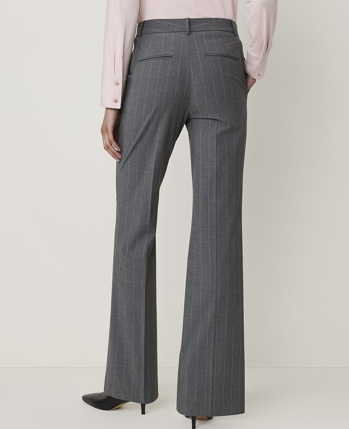 A person wearing gray pinstripe flared pants and a pink blouse stands against a plain, light-colored background.