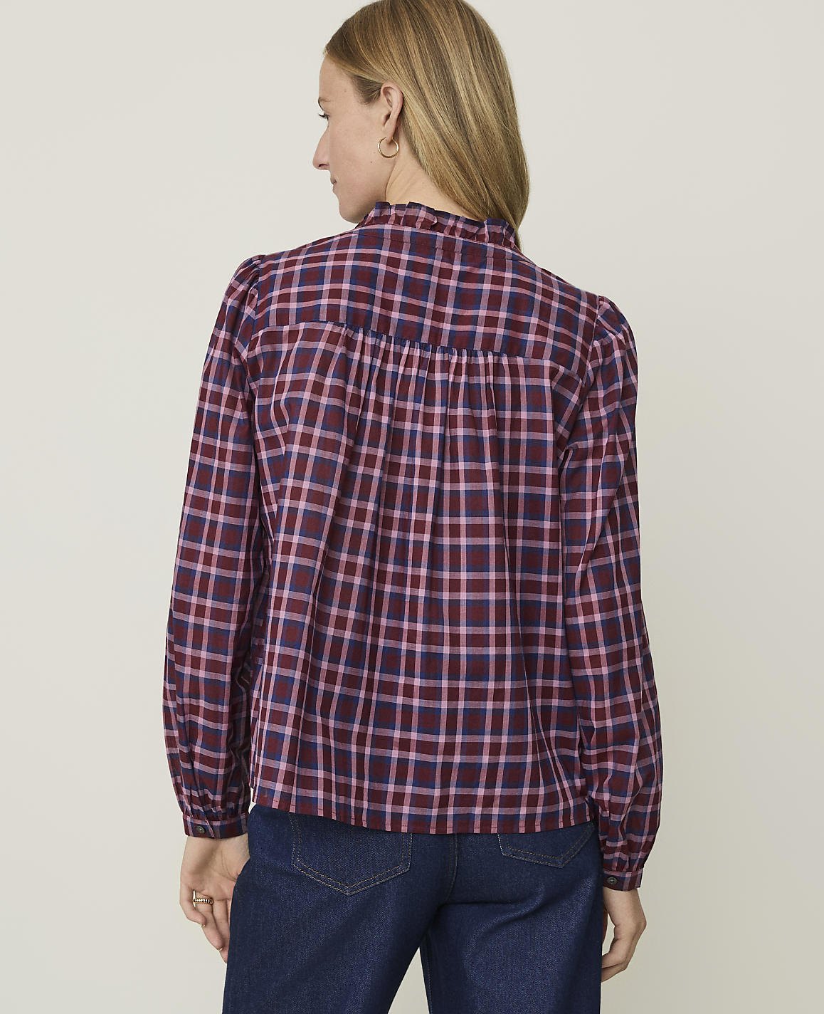 A woman in a maroon and pink plaid blouse stands against a plain, light-colored background.