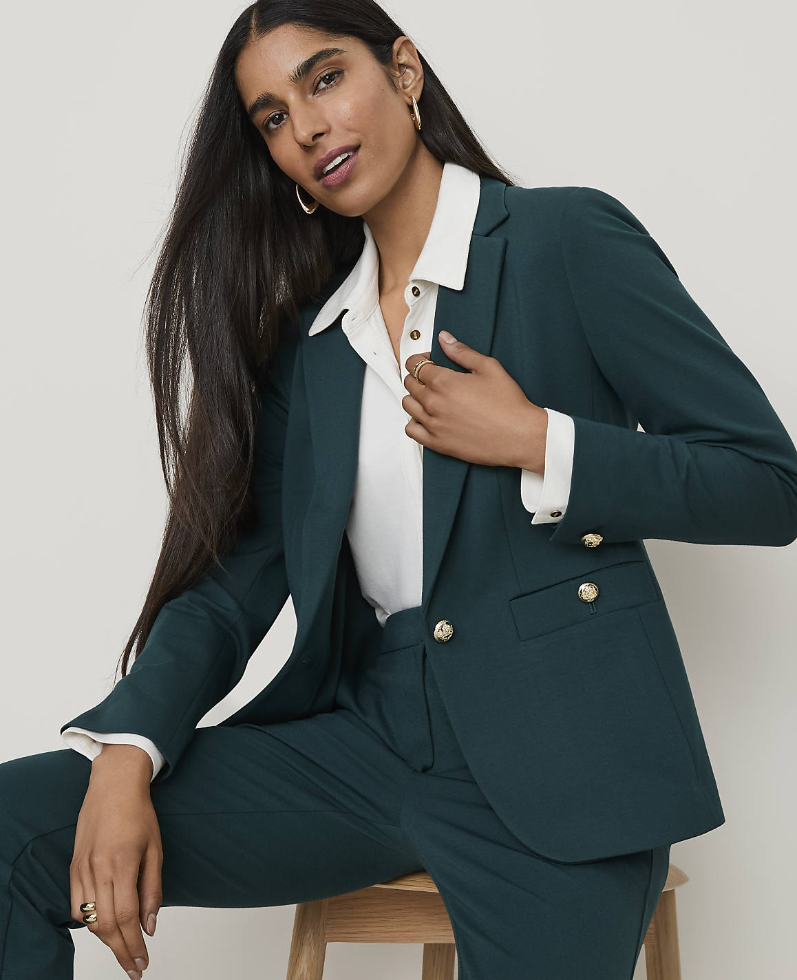 A woman in a teal blazer and pants poses against a plain, light background.