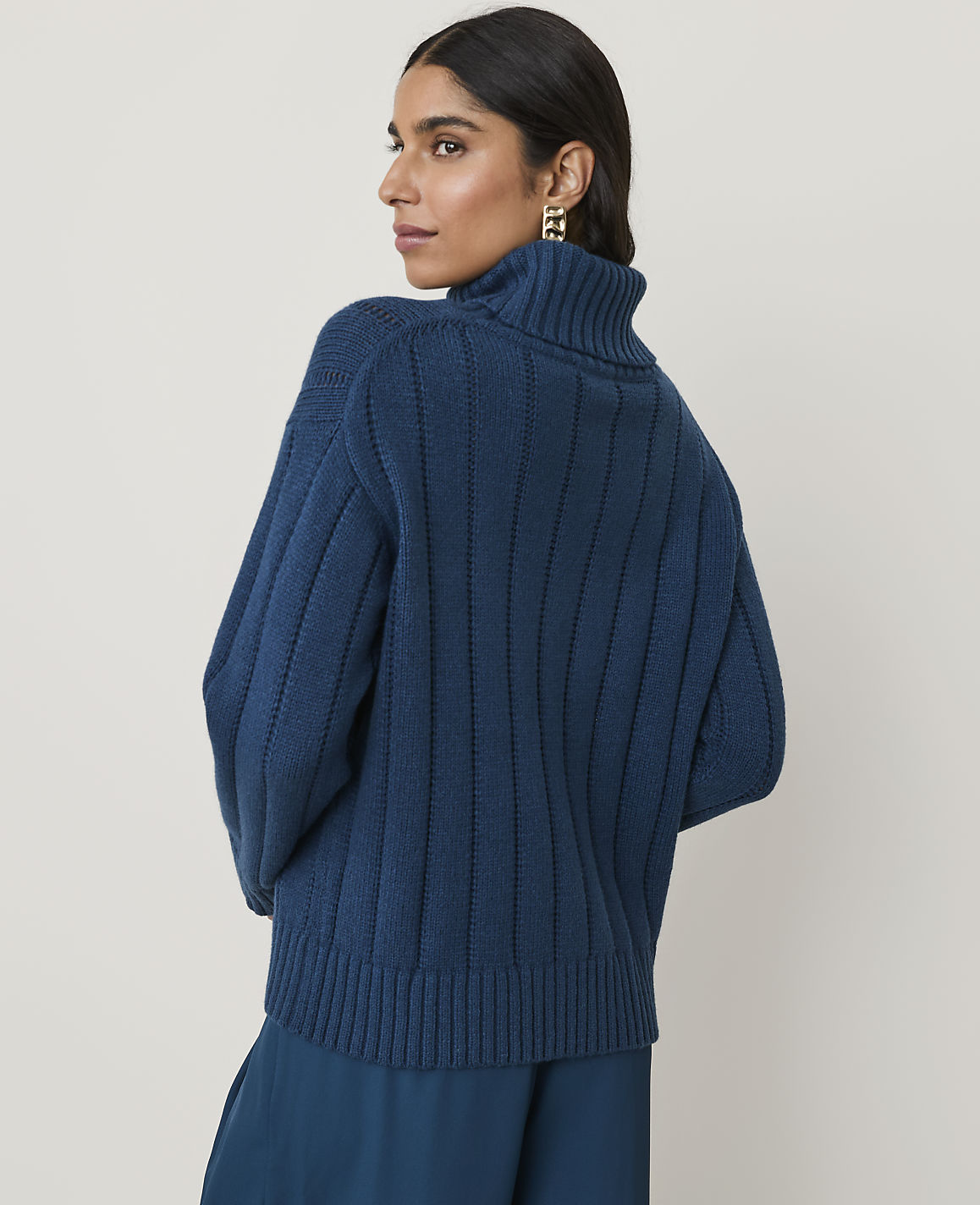 A woman in a teal turtleneck sweater stands against a plain, light background.