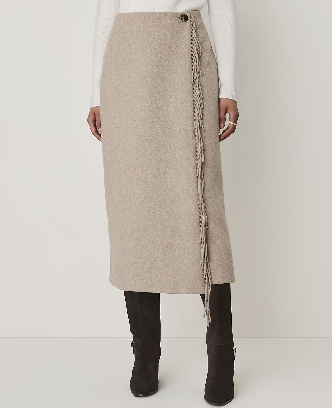 A beige wrap skirt with fringe detailing is worn over dark boots against a plain white background.
