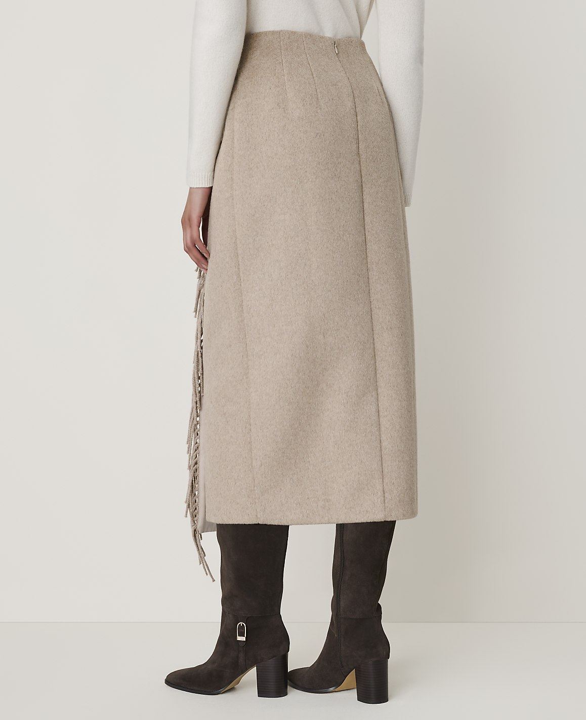 A beige midi skirt with fringe detailing is worn with dark brown boots against a plain white background.