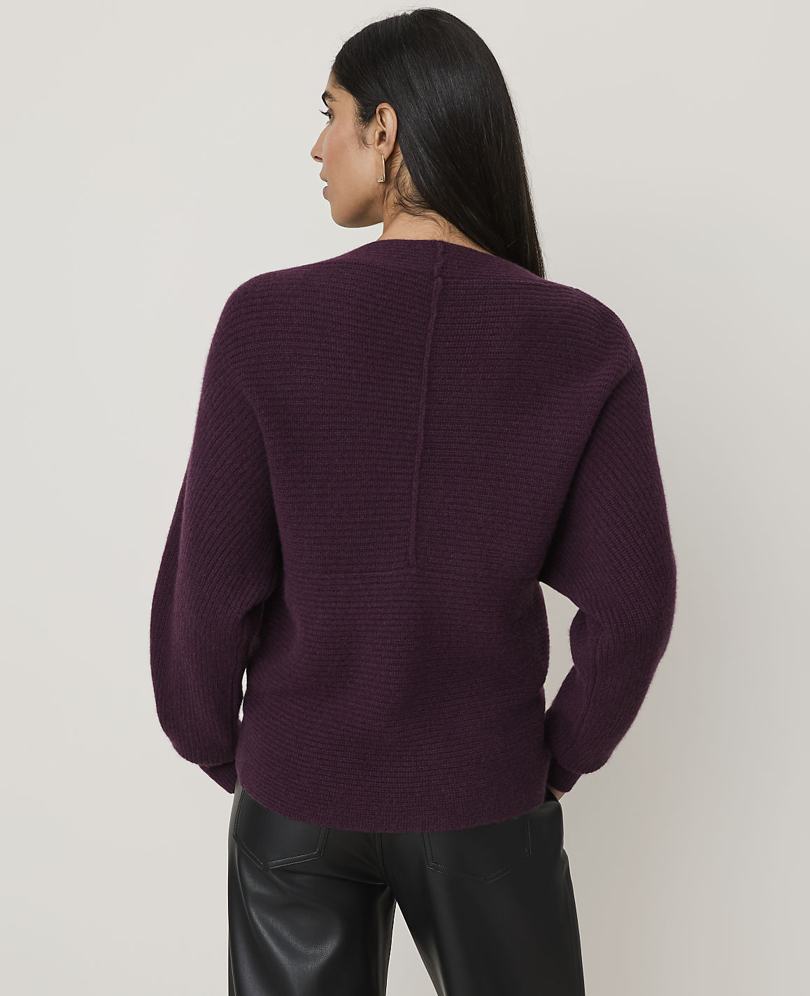 A woman in a burgundy ribbed sweater and black leather pants stands against a plain, light-colored background.