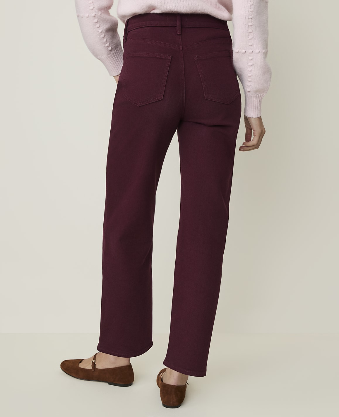 A person wearing burgundy pants and brown flats stands against a plain, light-colored background.