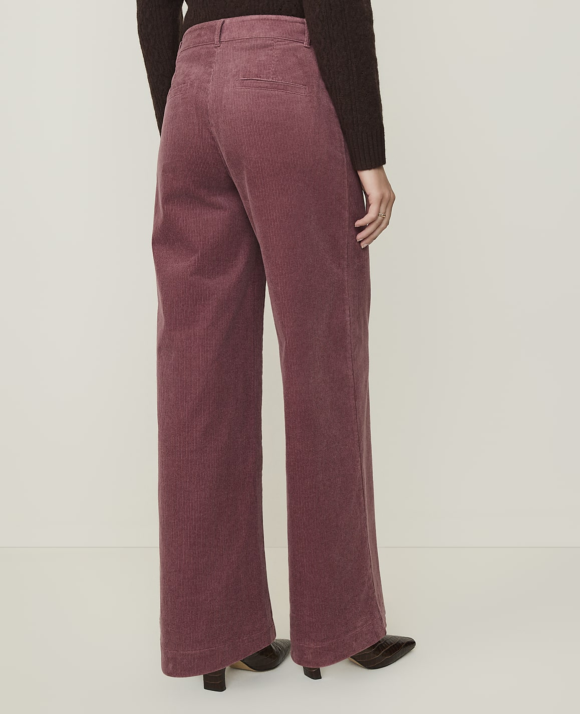 A person wearing rose-colored corduroy pants and dark shoes stands against a plain, light-colored background.