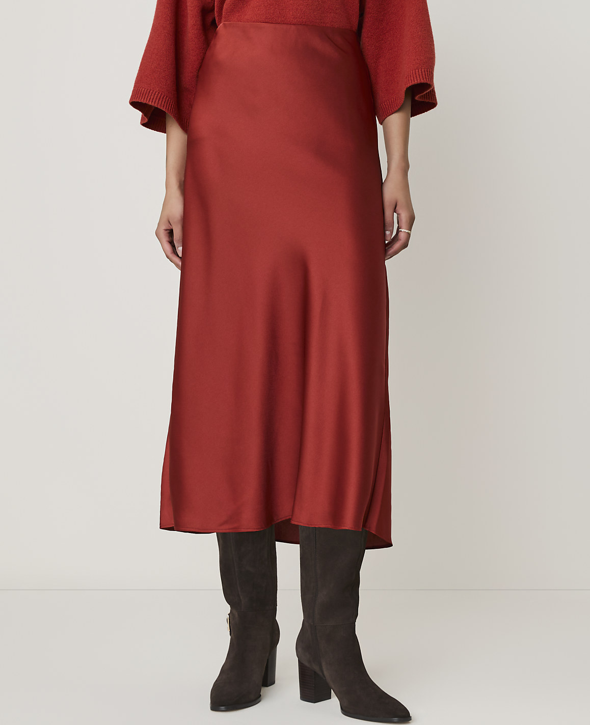 A person stands in a rust-colored satin skirt and dark boots against a plain white background.